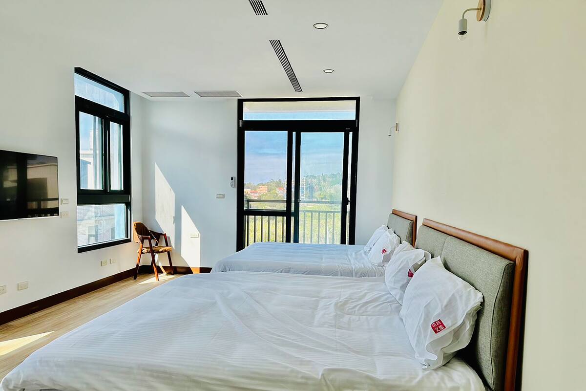 A modern bedroom with two beds, a TV, and a balcony with a view.