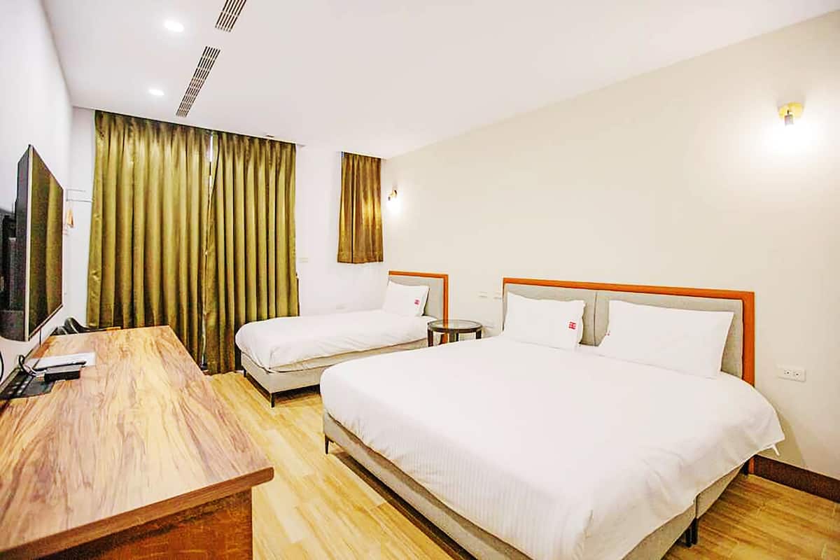 A hotel room with two single beds, a wooden desk, a flat-screen TV, and a large window with curtains.