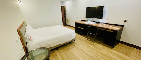 A hotel room with a bed, a desk, a chair, a TV, and a small table.