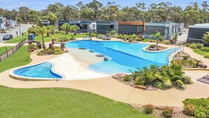 A swimming pool with a sandy edge, surrounded by a landscaped area with palm trees and rocks. - #56 Highview (Moama)
