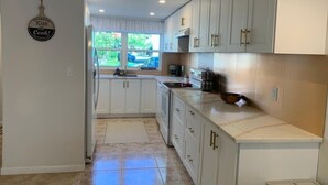 A kitchen with white cabinets, a window with a view of greenery, and a kitchen island with a microwave.