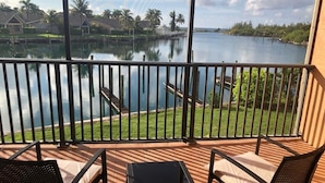 A balcony with a view of a lake, surrounded by greenery and houses.