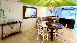 A dining area with a round table, white chairs, a wooden console table with decorative items, and a green ceiling.