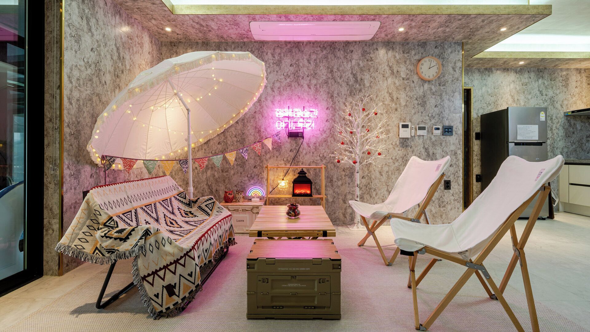 A cozy lounge area with a patterned sofa, a white folding chair, a small table, and a decorative umbrella.