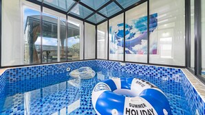En inomhuspool med blå mosaikplattor, väggar av genomskinligt glas och en uppblåsbar badring med sommarlovsmotiv.