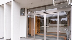 A modern building entrance with glass doors, a tiled floor, and a visible interior with shelves and a sign. - Hirononomori Maehama Bekkan - Male only (Hirono)