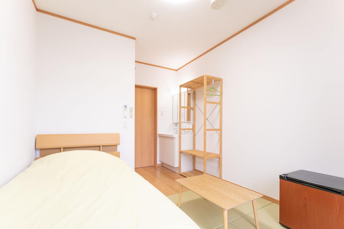 Une pièce comprenant un lit, un banc en bois, une armoire et une étagère avec un cintre vert.