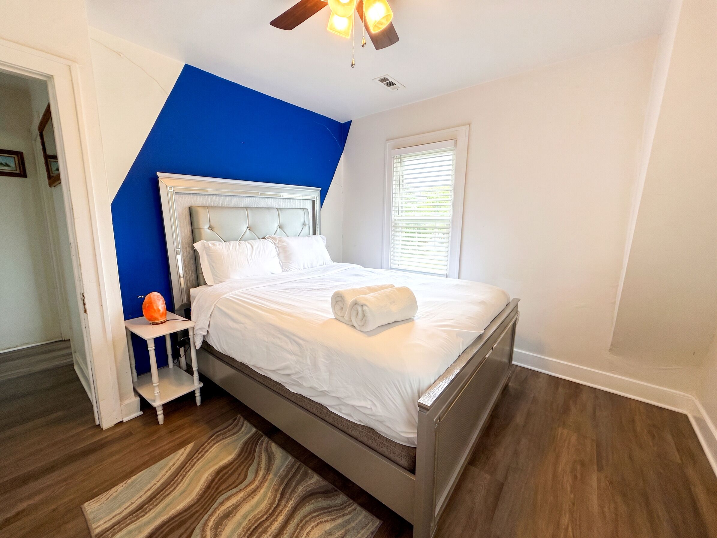 A bedroom with a bed, a nightstand, a ceiling fan, and a window with blinds.