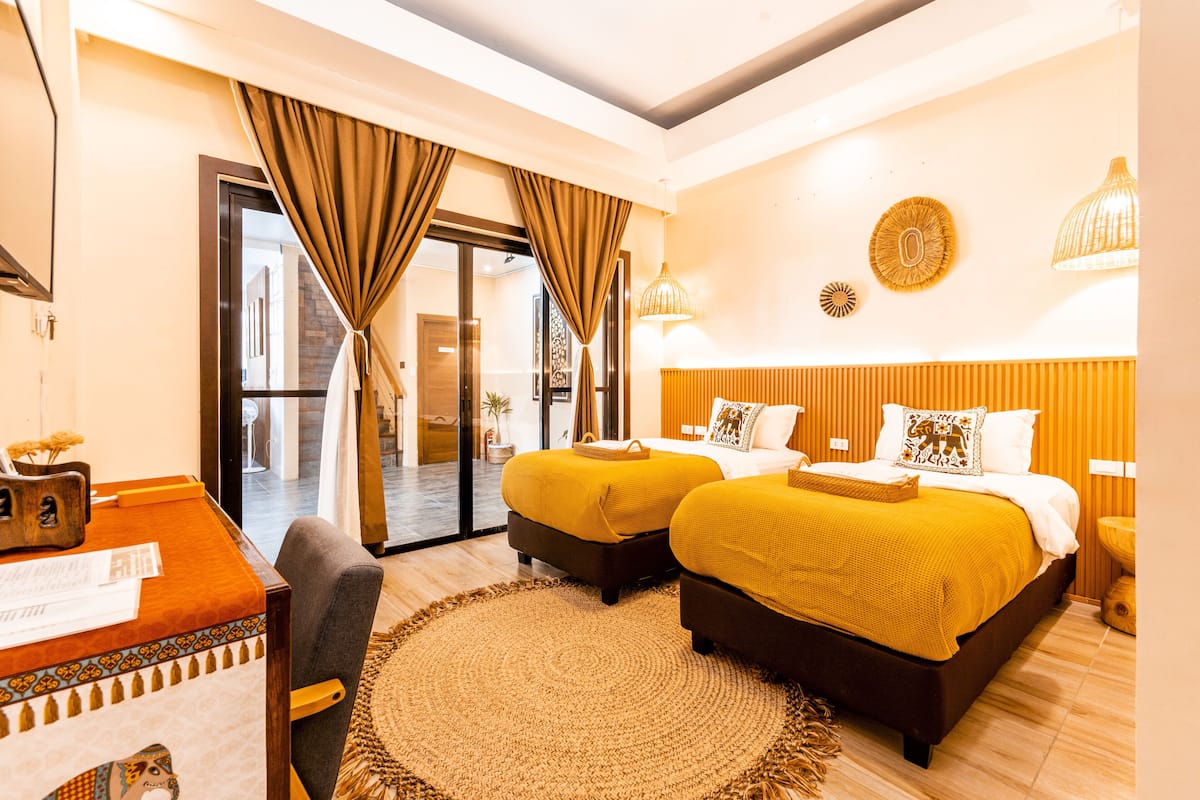A hotel room with two beds, a desk, and a large window with curtains.