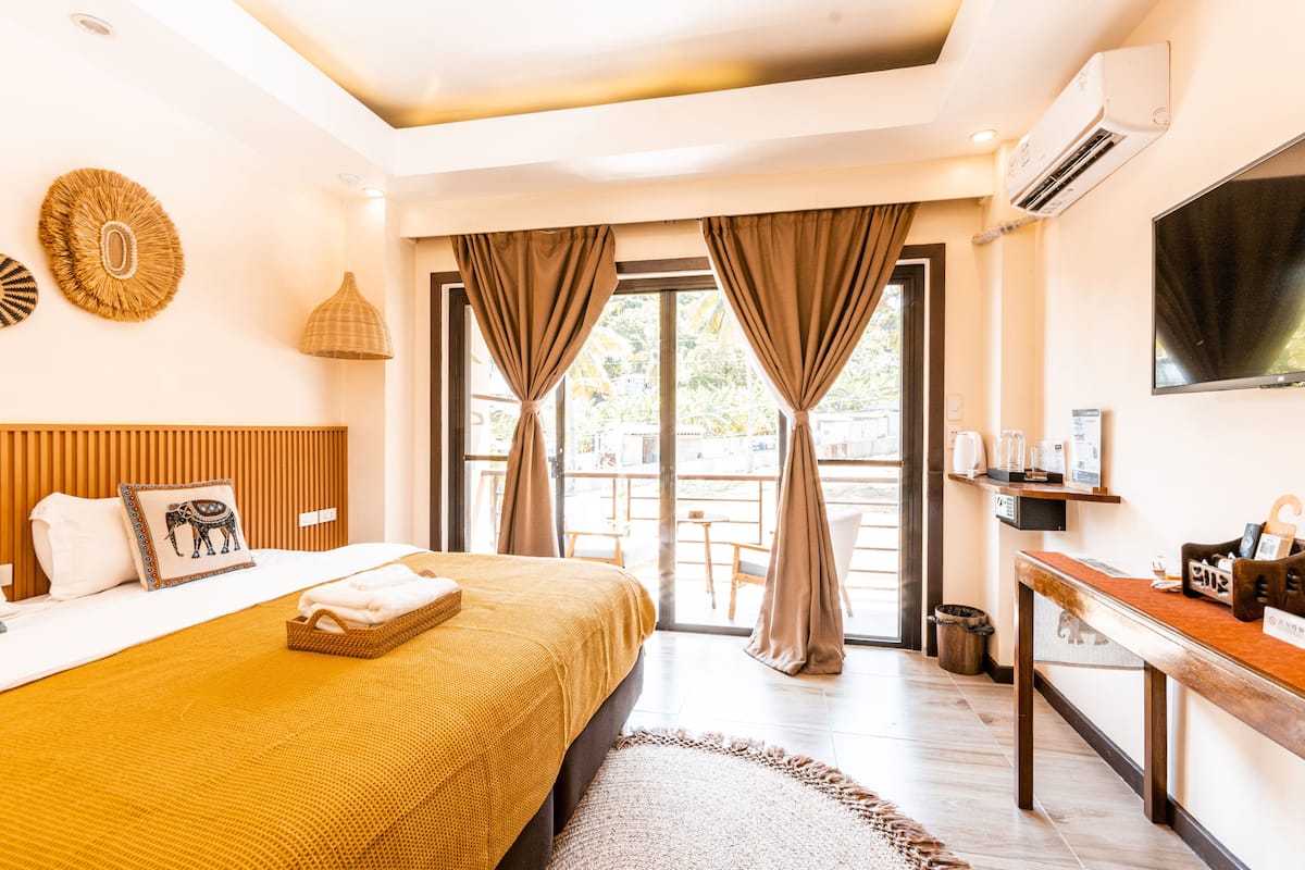 A hotel room with a large bed, a desk, a TV, and a balcony with curtains.