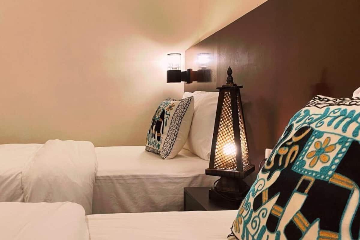 A hotel room with a bed, a nightstand, a wall-mounted lamp, and a decorative pillow.