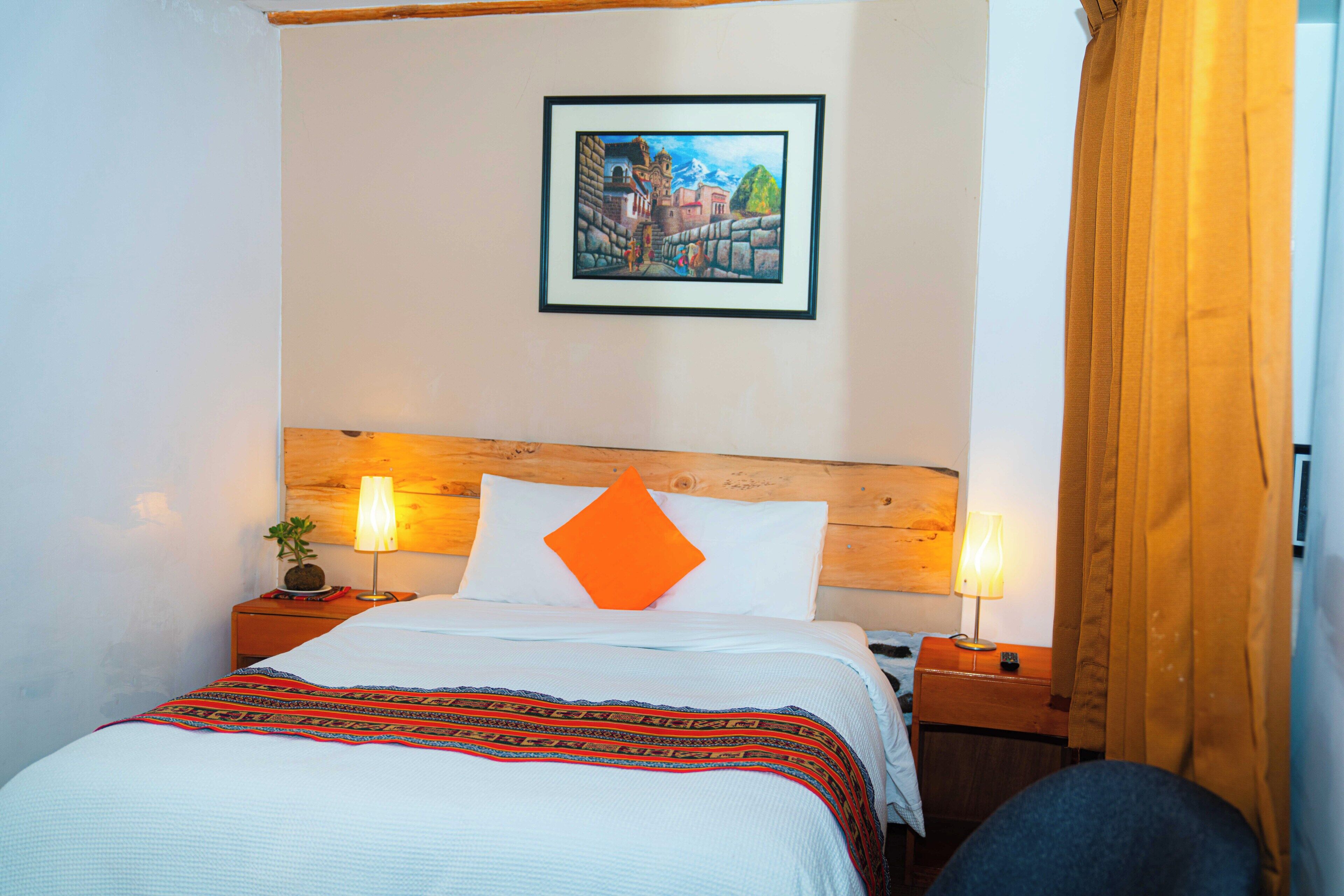 A hotel room with a bed, two bedside tables, a nightstand, a lamp, a framed picture on the wall, and a curtain.