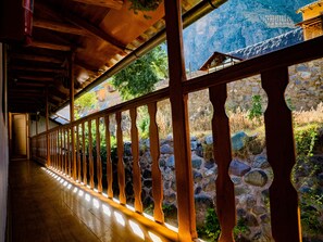 A corridor with wooden railings, a stone wall, and a view of a mountainous landscape.