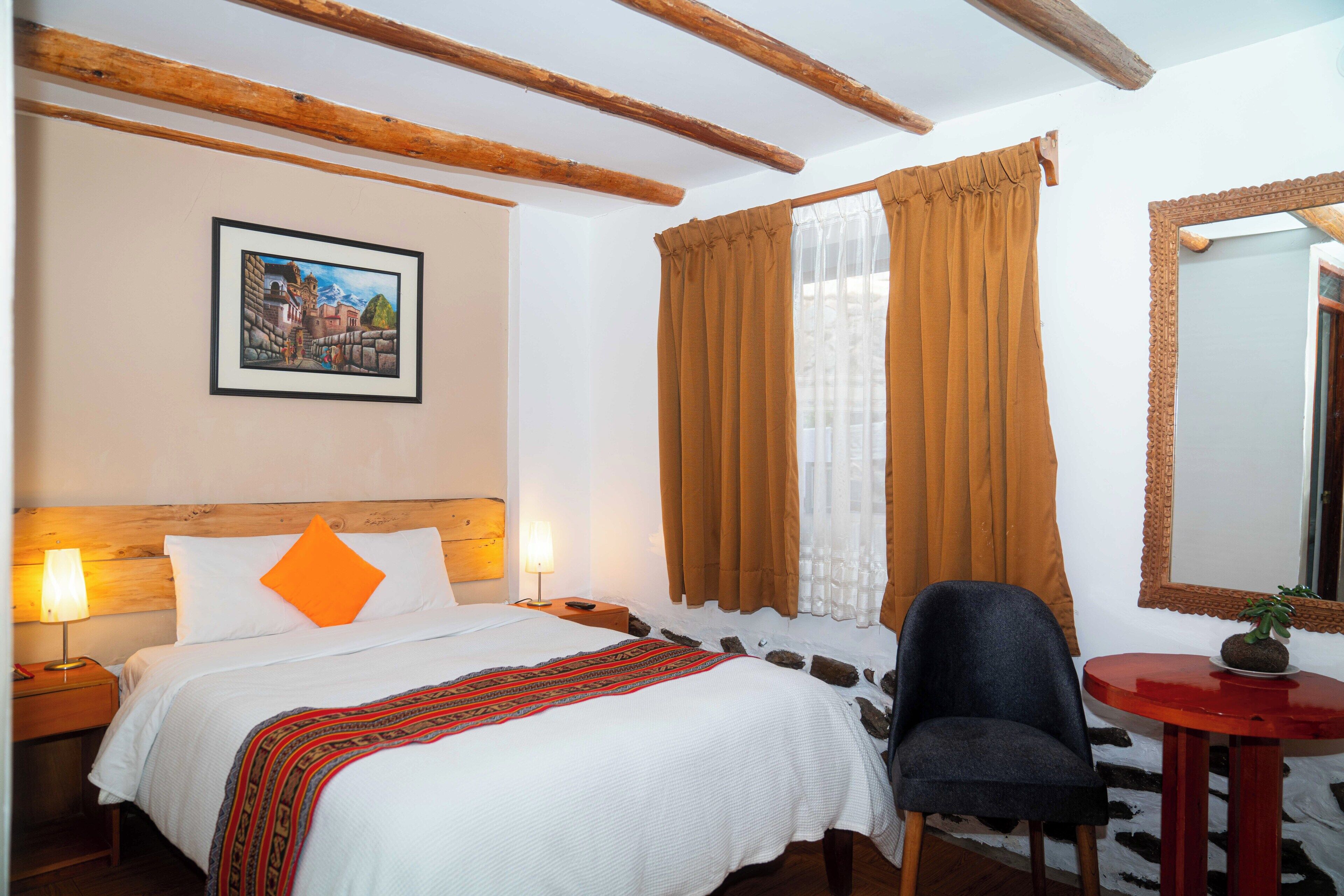 Une chambre d’hôtel avec un lit, une chaise, une petite table, un miroir et un tableau au mur.