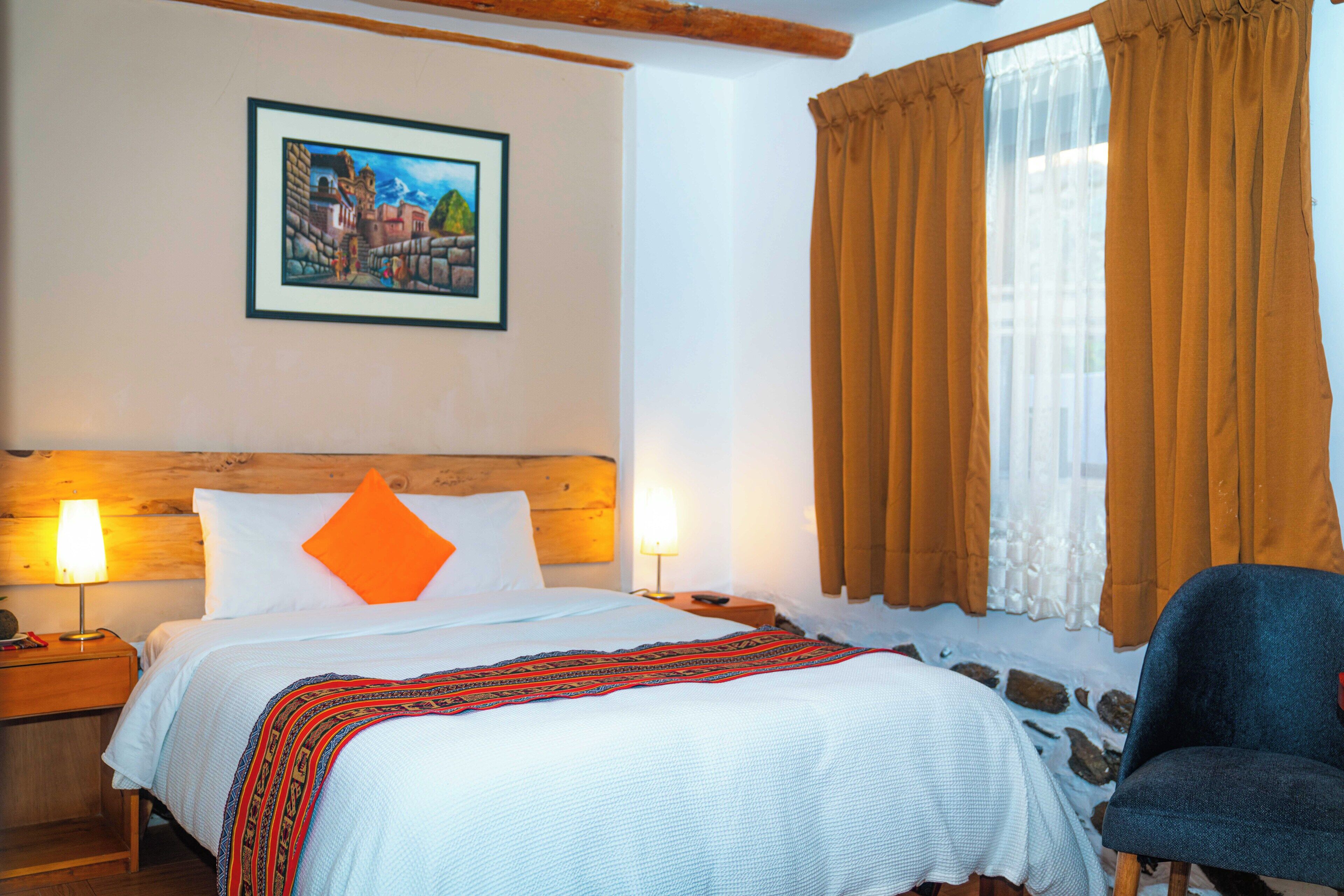 A hotel room with a bed, a nightstand with a lamp, a chair, and a window with curtains.