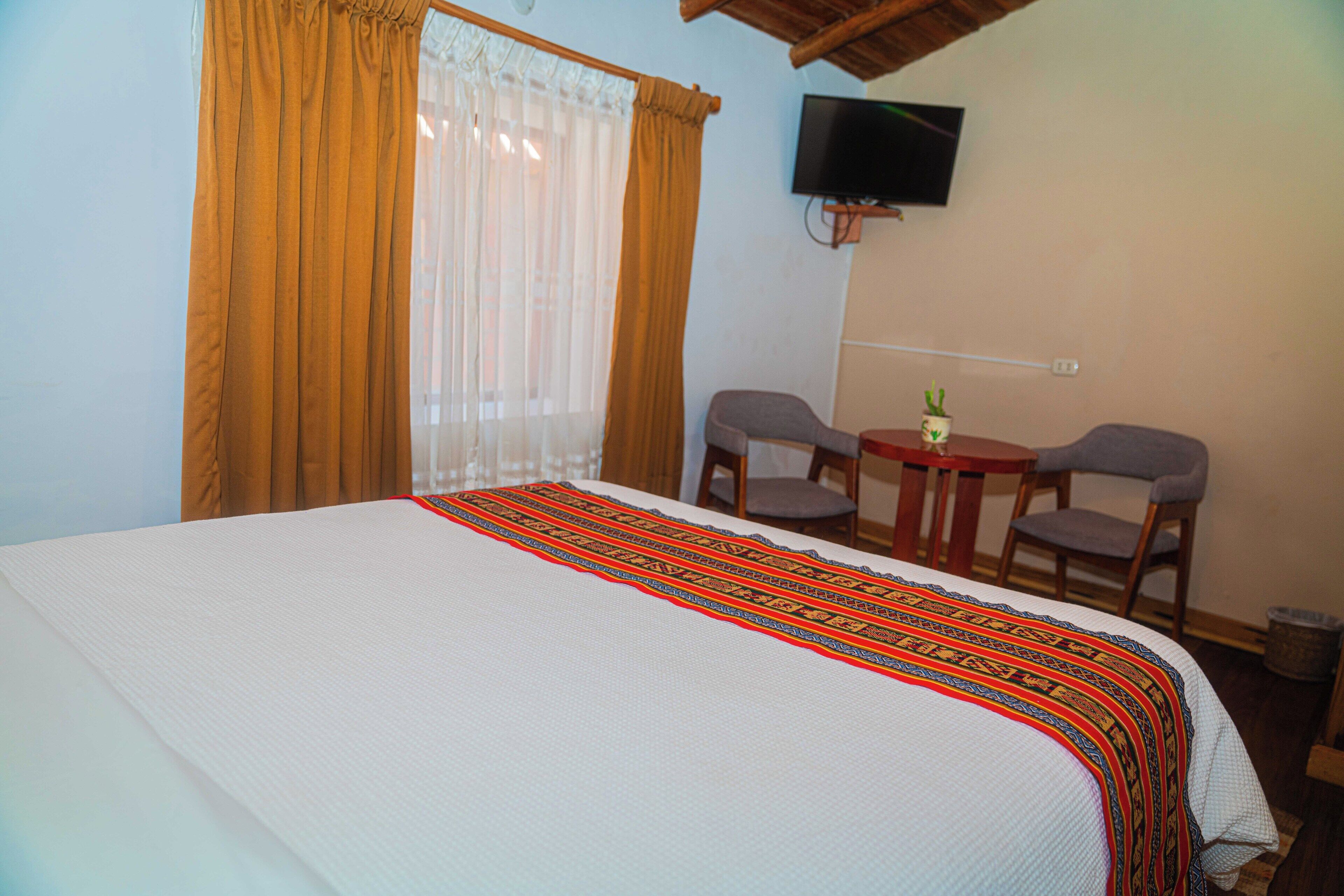Una habitación de hotel con una cama grande, un televisor montado en la pared, dos sillas y una mesita.