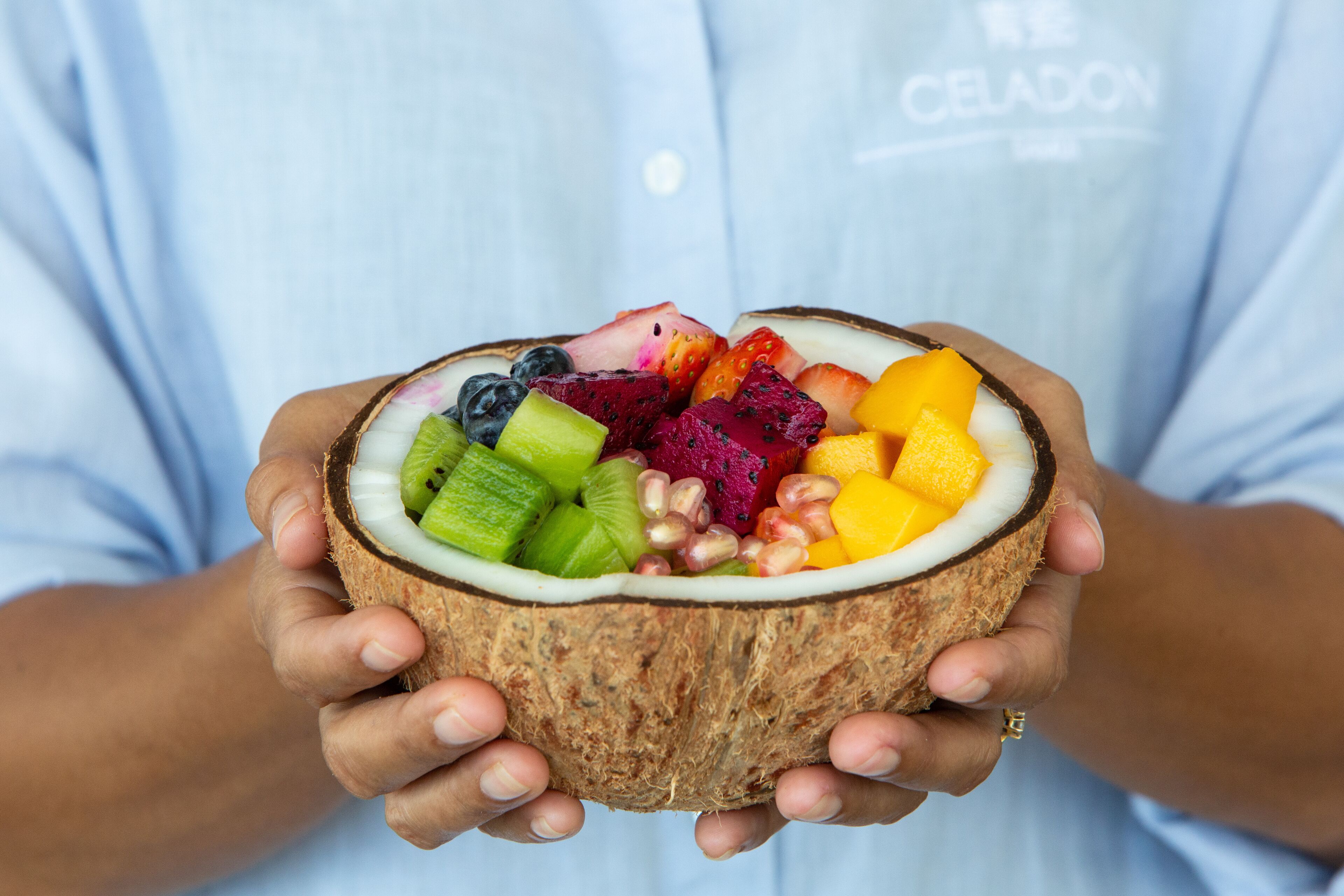 A person holding a coconut filled with various fruits.