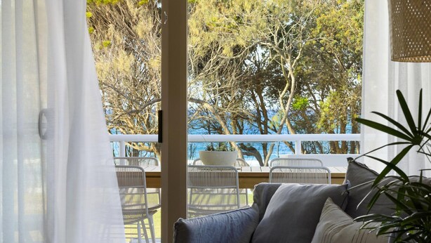 A room with a view of trees and a body of water through large windows. - Oceanfront Byron Palms - 2 BR Main Beach apartment (Byron Bay)