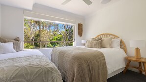 A bedroom with two beds, a large window with a view of trees, and a wooden headboard. - Oceanfront Byron Palms - 2 BR Main Beach apartment (Byron Bay)