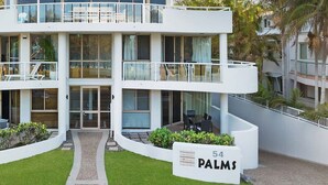 A modern multi-story hotel with a white facade, a covered outdoor seating area, and a sign indicating the name '54 PALMS'. - Oceanfront Byron Palms - 2 BR Main Beach apartment (Byron Bay)