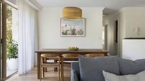 A dining area with a wooden table, two chairs, a bowl of lemons, and a hanging wicker light fixture. - Oceanfront Byron Palms - 2 BR Main Beach apartment (Byron Bay)