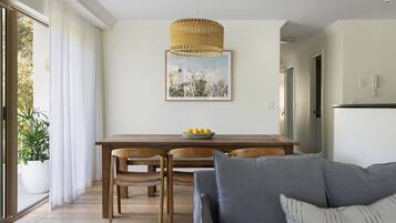 A dining area with a wooden table, two chairs, a bowl of lemons, and a hanging wicker light fixture.