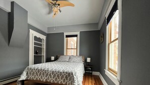 Una camera da letto con un letto, un comodino, una ventola a soffitto e una finestra.