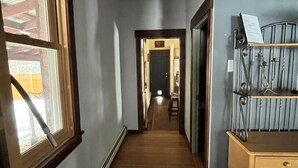 Un corridoio stretto con pavimento in legno, una finestra a sinistra e un mobiletto a scaffali in metallo a destra.