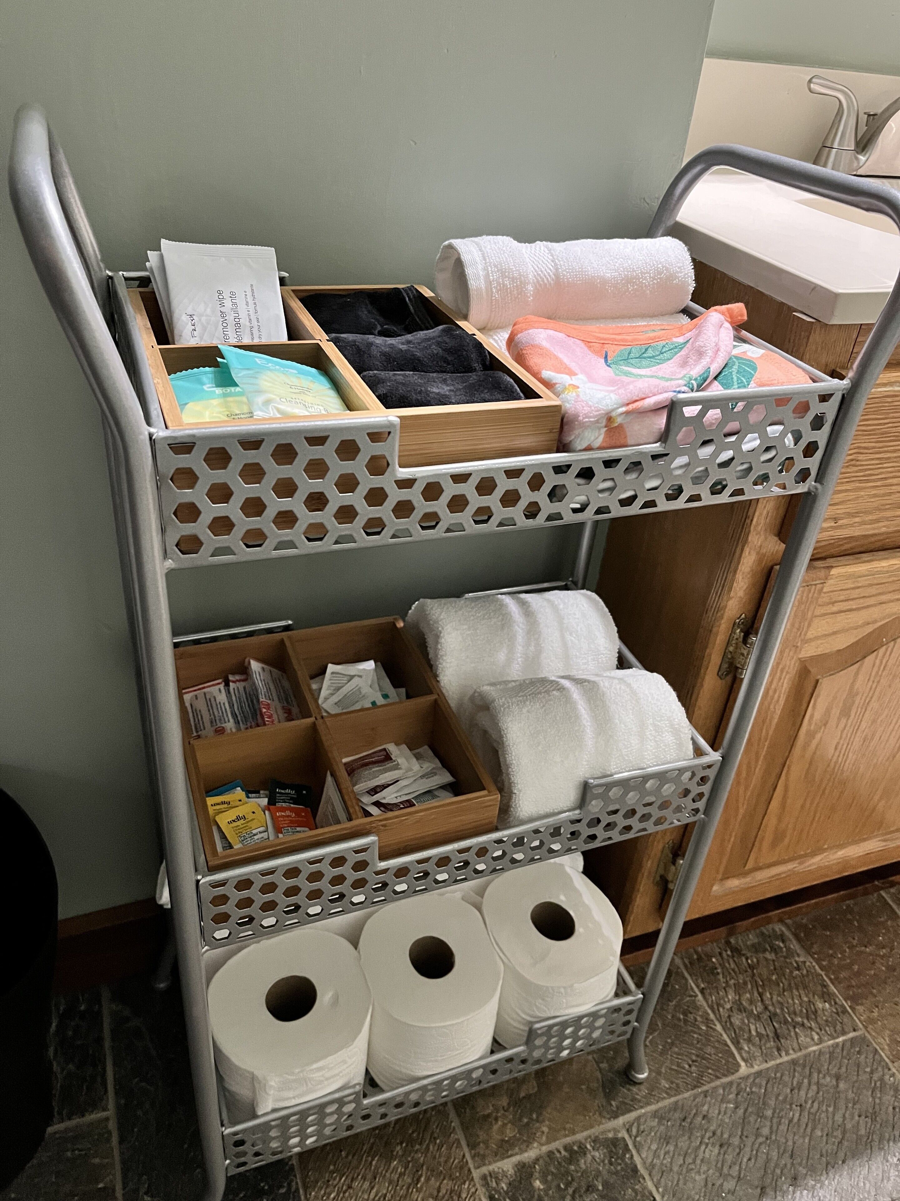 Un chariot en métal doté de plusieurs compartiments pour ranger les articles de toilette, les serviettes et les produits en papier.