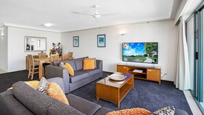 Een moderne woonkamer met een grijze bank, een houten salontafel en een flatscreen televisie.