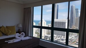 Een hotelkamer met een bed, een lamp en uitzicht op hoge gebouwen en de oceaan.