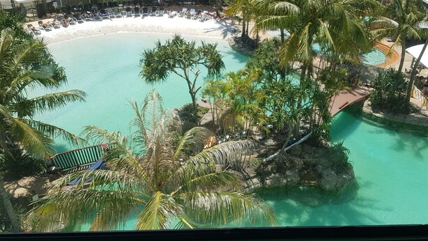 Een resort met een groot zwembad, omringd door palmbomen en een strand.