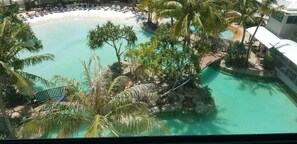 Een resort met een groot zwembad, omringd door palmbomen en een strand.