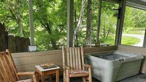 Un espace extérieur abrité comprenant deux fauteuils à bascule en bois, une petite table et un jacuzzi.