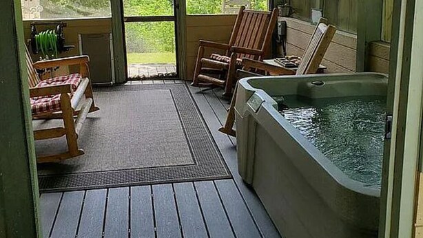Une véranda couverte avec un plancher en bois, un jacuzzi et deux fauteuils à bascule.