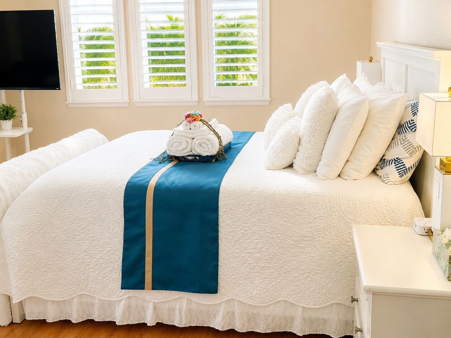 A neatly made bed with a blue and white bedspread, a set of white pillows, and a basket of rolled towels.