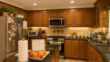 A kitchen with wooden cabinets, a stainless steel refrigerator, a microwave, a stove, and various kitchen appliances.
