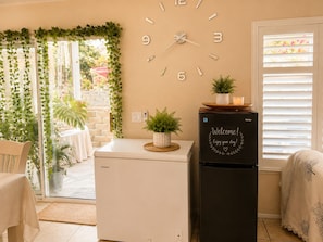 A room with a clock on the wall, a refrigerator with a welcome message, and a view of a garden through a glass door. - Balloons and Wine (Murrieta)