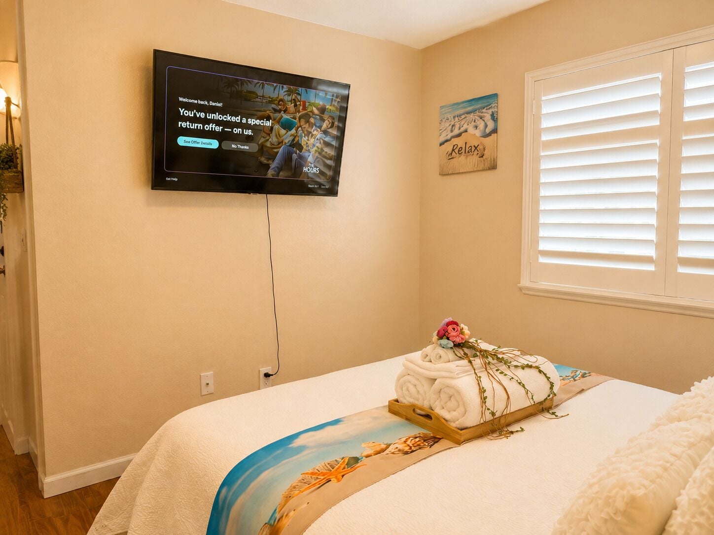 Habitación de hotel con cama, televisor montado en la pared, ventana con persianas y una decoración en la pared.
