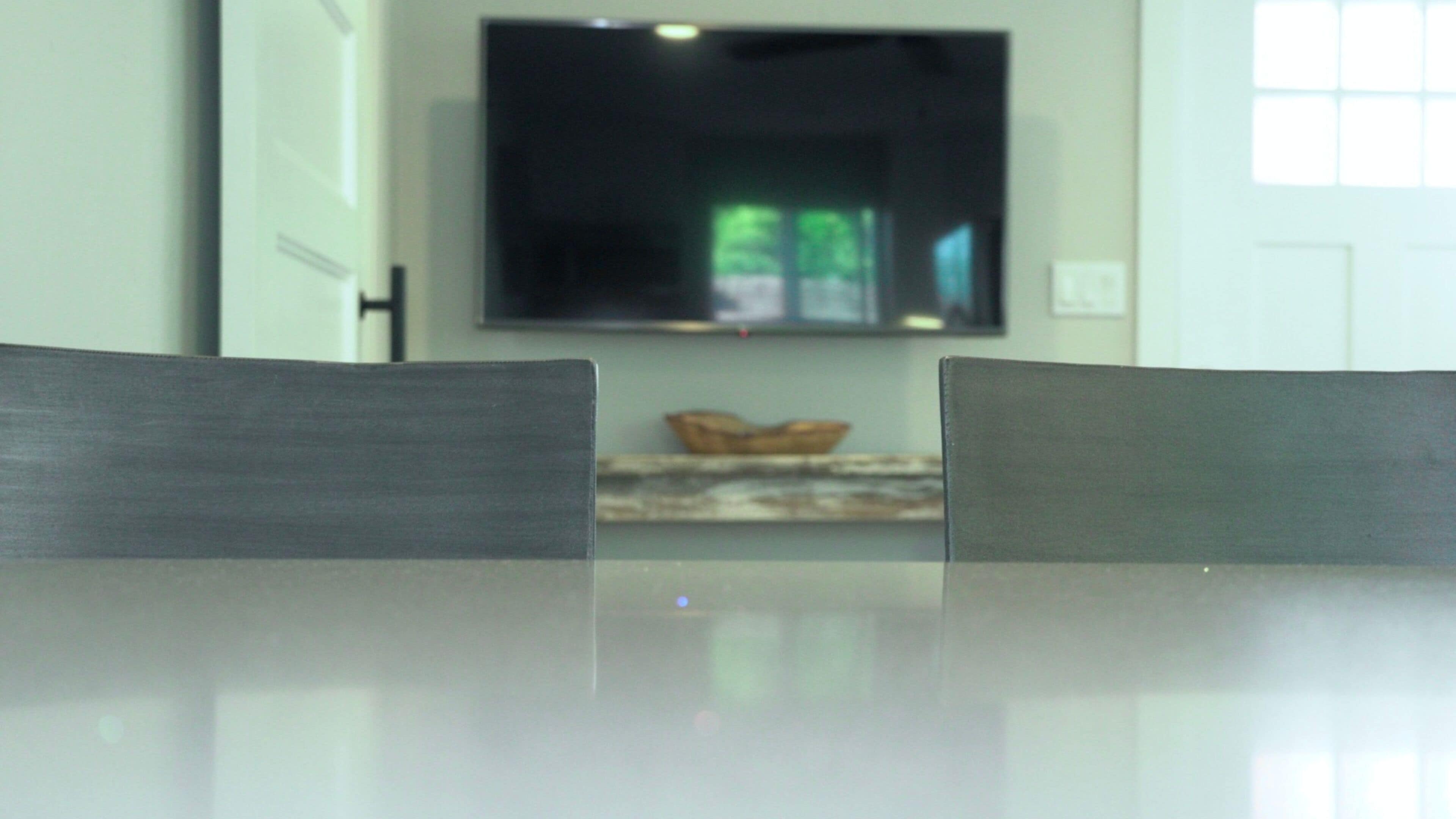 A dining area with a table and two chairs, a flat-screen TV mounted on the wall, and a basket on the table.