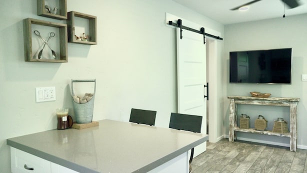 Una cocina con una isla grande, una puerta corredera, un televisor montado y un rústico aparador de madera.