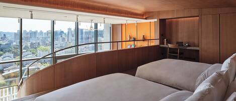 A modern bedroom with a curved ceiling, large windows offering a city view, and a built-in desk with a chair.