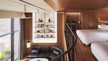 A modern hotel room with a wooden ceiling, a large window, a leather sofa, a round table, and a bed with white linens.