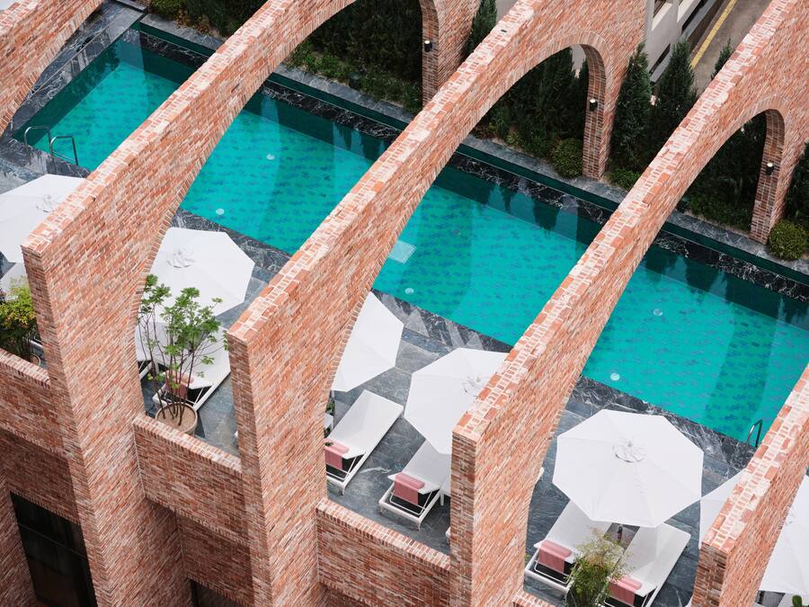 A rooftop pool with clear blue water, surrounded by brick walls and white umbrellas.