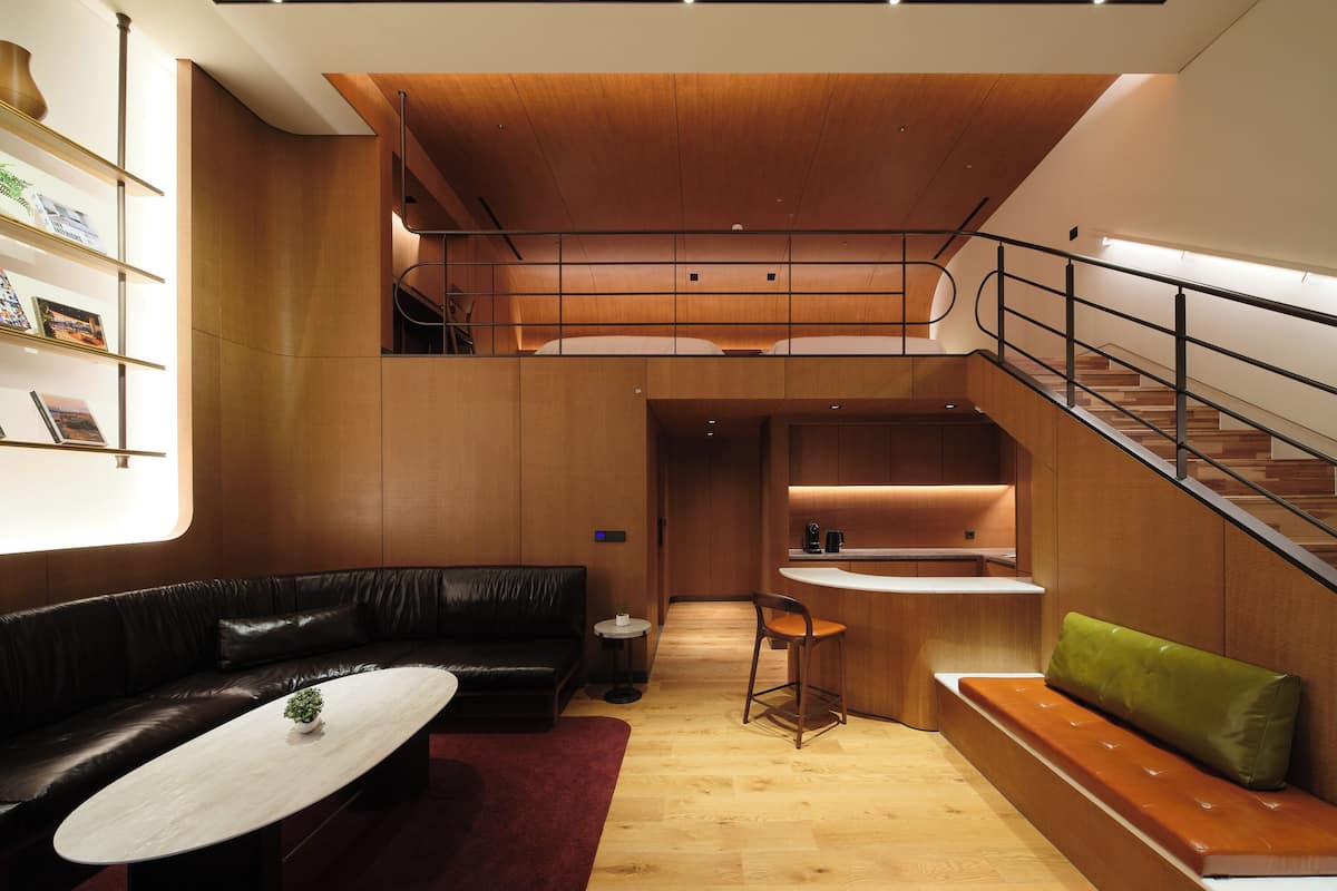A modern interior with a wooden ceiling, a black leather sofa, a round table, and a staircase.