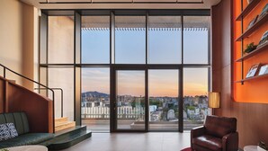 A modern interior with a large window, a staircase, a sofa, a red rug, and a bookshelf. - ANANTI AT GANGNAM (Seoul)