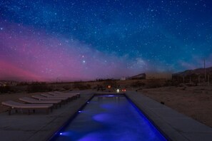 Une piscine dotée de chaises longues et offrant une vue sur le ciel nocturne.