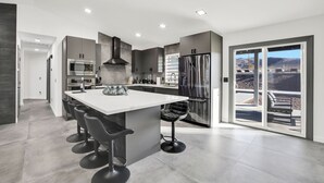 A modern kitchen with a central island, bar stools, and a view of the outdoors through large sliding doors.
