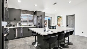 A modern kitchen with stainless steel appliances, a large island with bar stools, and a view of the outdoors through the window.