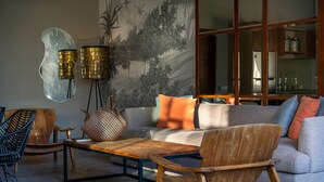 A modern living room with a sofa, two wooden chairs, a coffee table, and a wall-mounted lamp. - Private Pool • Garden Views • Two King Bedrooms (Canggu)